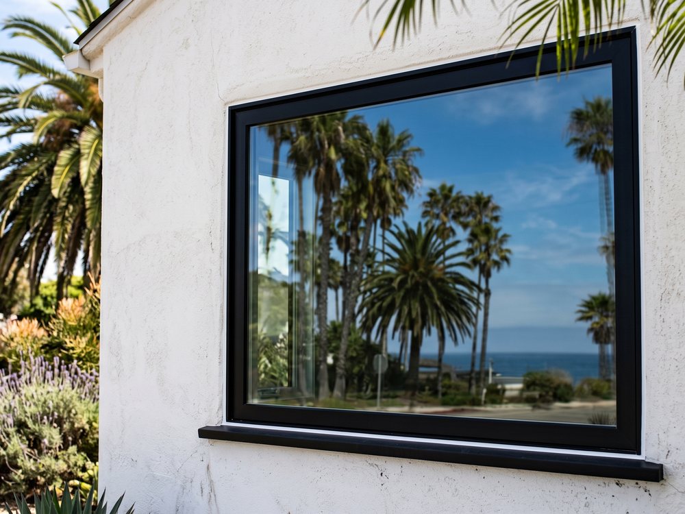 New black framed window on a white stucco coastal home with ocean reflection